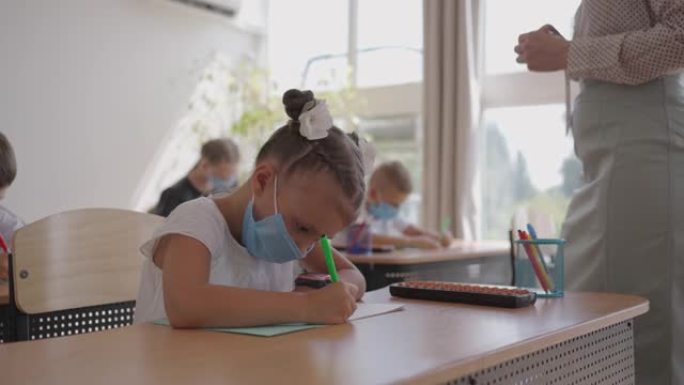 戴防护面具的学生在电晕病毒大流行期间在学校学习。一位蒙面老师向蒙面学生讲解了一个新的课程主题。孩子们