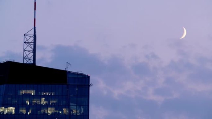 黄昏时现代摩天大楼顶部的空中拍摄，带有可见的新月