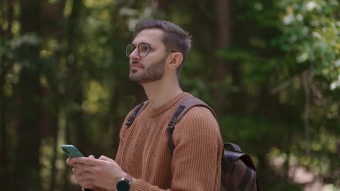 一个背着背包的男性旅行者沿着森林中的一条土路行走，写信息，在互联网上交流，查看内容，在手机上做笔记，