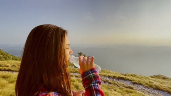 SLO MO女徒步旅行者在阳光明媚的山坡上喝水