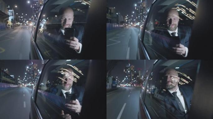 夜间穿越城市。商人在后座上使用智能手机