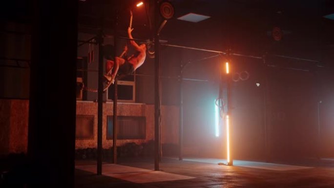 健身男子在健身房做攀绳运动。橙蓝色霓虹灯。一名男子在健身房攀岩