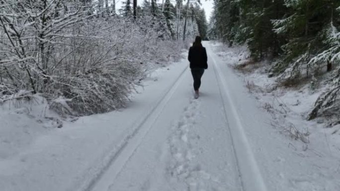 空中无人机拍摄了一名妇女在树林中沿雪道行走的镜头