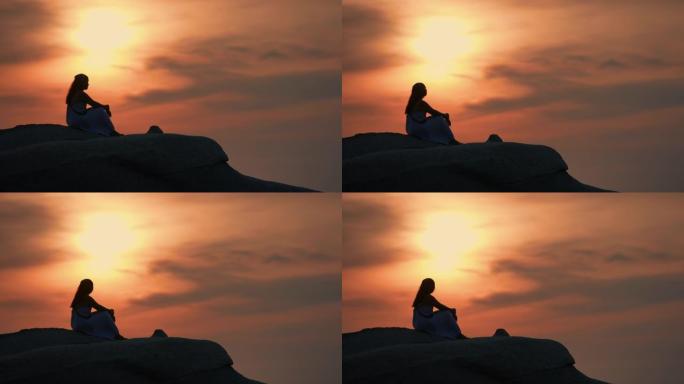 日落时在山顶上放松的年轻女子