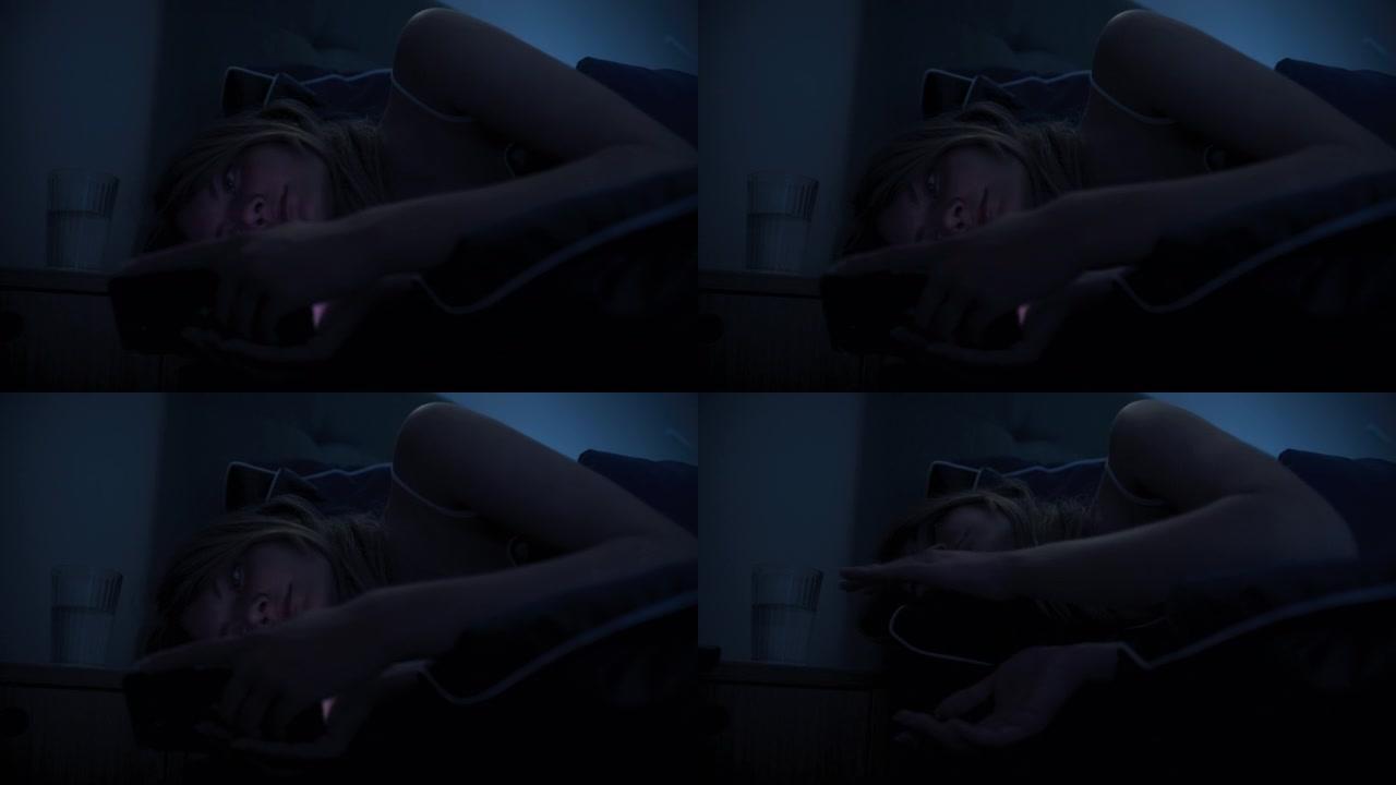 躺在床上的女人因失眠而无法入睡。检查电话