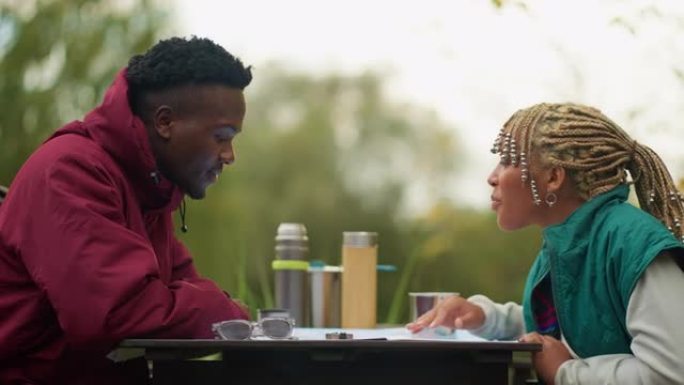 非洲族裔少年夫妇看着地图和指南针，从北欧人在公园餐桌上散步休息。