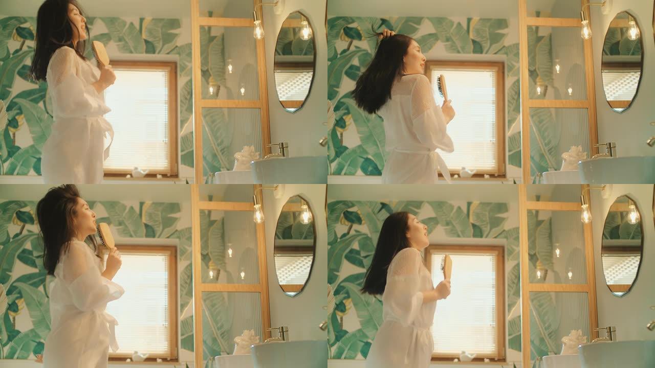 感觉棒极了。亚洲女性享受早上的浴室活动，在镜子前玩得开心。对着发刷唱歌，用力跳舞