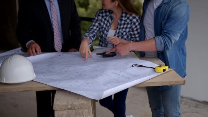 房地产开发商和夫妇在简易桌子上看着新房建筑工地的蓝图