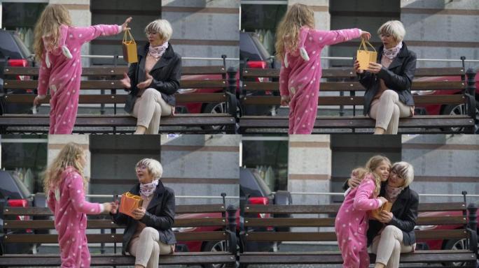 迷人可爱的孙女在阳光明媚的城市街道上给祖母惊喜。快乐微笑的高加索高级女人拥抱漂亮女孩说话的肖像。休闲