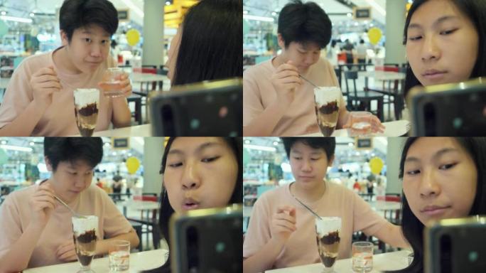 亚洲女孩使用移动相机为在餐厅吃冰淇淋的哥哥拍照。