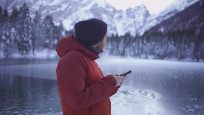 年轻人在白雪皑皑的湖边用手机发短信