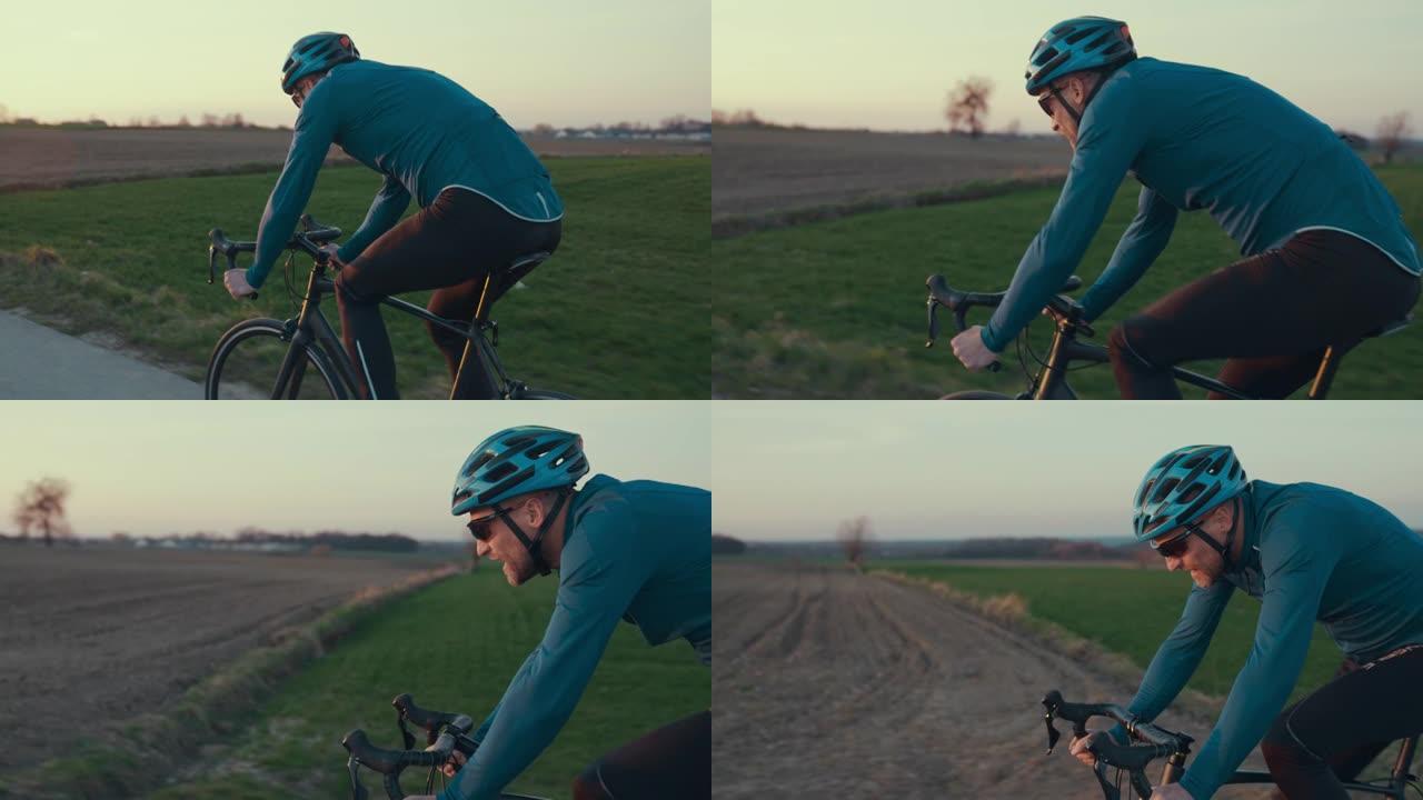 男性公路自行车手在空旷的地方超速行驶的后视图。春天的日落