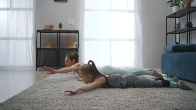 年轻的母亲和小女儿的体操训练，躺在房间的地板上，躯干上升，运动家庭