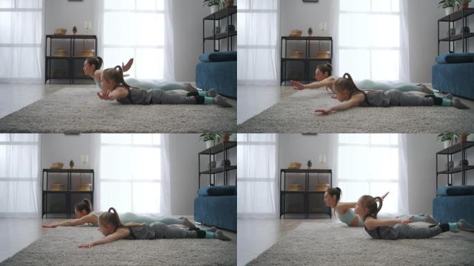 年轻的母亲和小女儿的体操训练，躺在房间的地板上，躯干上升，运动家庭