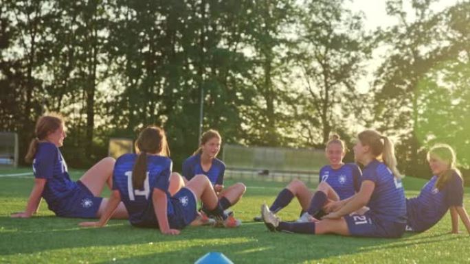 足球队的女孩在练习和大笑后坐在运动场上
