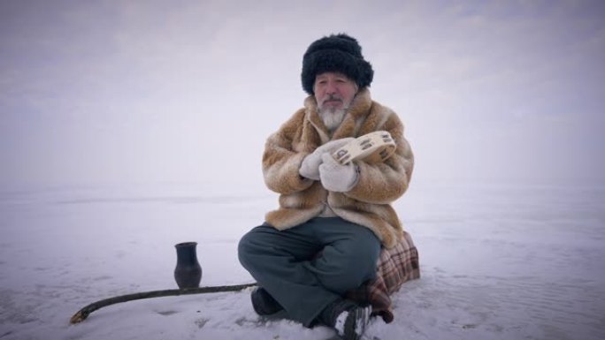 集中的萨满鼓鼓手鼓坐在冰冻的北冰洋上。宽幅自信的资深土著男子在风景如画的户外祈祷。灵性概念。