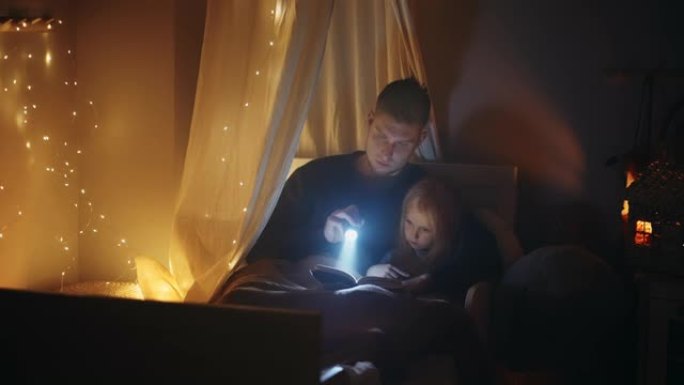 细心的父亲和小女孩晚上睡觉时在黑暗的卧室里读童话故事