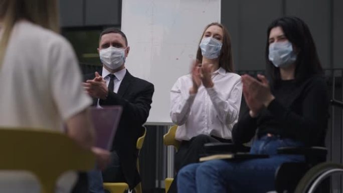 冠状病毒的同事戴着口罩，以慢动作鼓掌，作为发言人，介绍有关新型冠状病毒肺炎大流行爆发的商业报告。高加