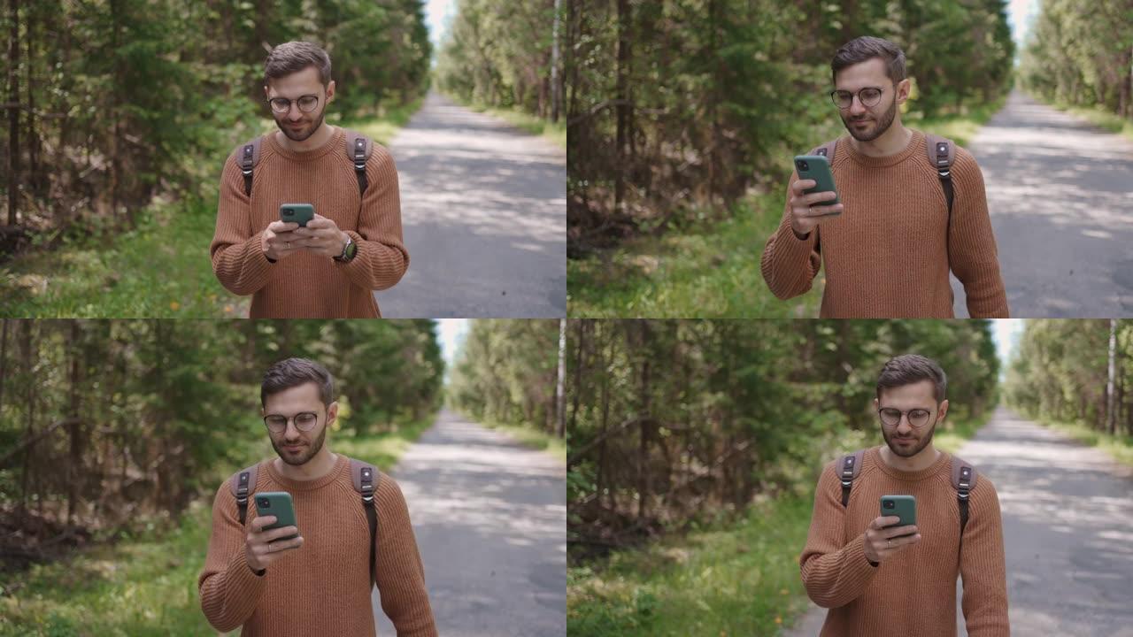 一个背着背包的年轻人沿着森林地区的道路行走，写信息，在互联网上交流，查看内容，在线搜索信息，微笑。