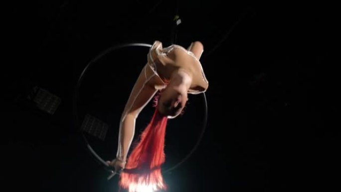 微笑美女挂在气环上的底角视图，黑色背景背光。红发诱人的高加索灵活体操运动员在舞台上慢动作表演的肖像。