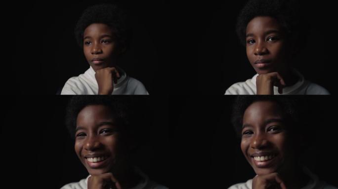 一个黑人男孩在黑色背景下看着相机的特写肖像