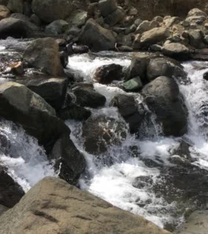 从右到左平移的水沿着悬崖底部从岩石清澈的小溪翻滚