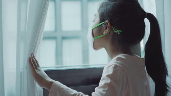 戴着面具的小女孩透过窗户看着家里的检疫。