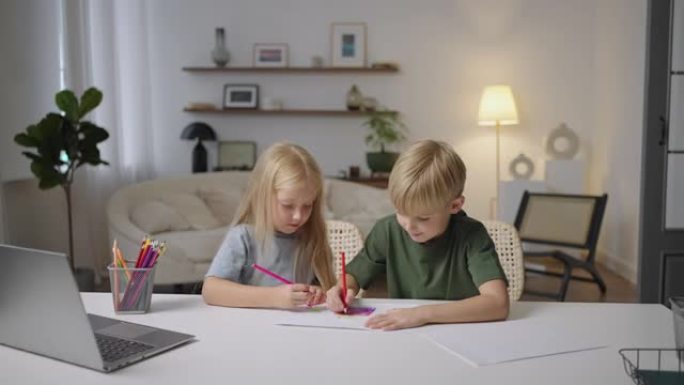两个金发孩子，一个男孩和一个女孩，看着笔记本电脑屏幕，坐在桌子旁执行教师任务，远程学习外语，以游戏形
