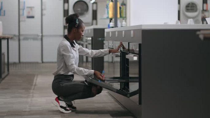 年轻的非洲裔美国女士正在五金店观看现代烤箱，为新公寓选择设备