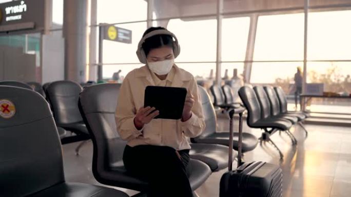 亚洲妇女在机场出发区使用数字平板电脑戴口罩。