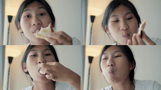 亚洲女孩通过智能手机观看电影或病毒视频，并在周末在家窗口附近吃三明治。