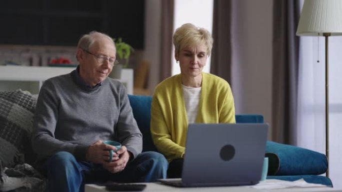 开朗的老年男女正在通过笔记本电脑与朋友或家人进行视频聊天，周末坐在家里的客厅里