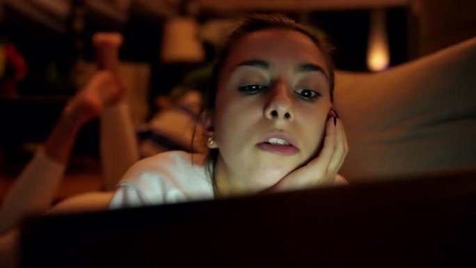 美丽的年轻女子在沙发上放松。在笔记本电脑上观看有趣的电影