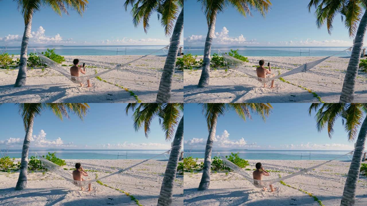 男子坐在海滩上两棵棕榈树之间的吊床上打电话