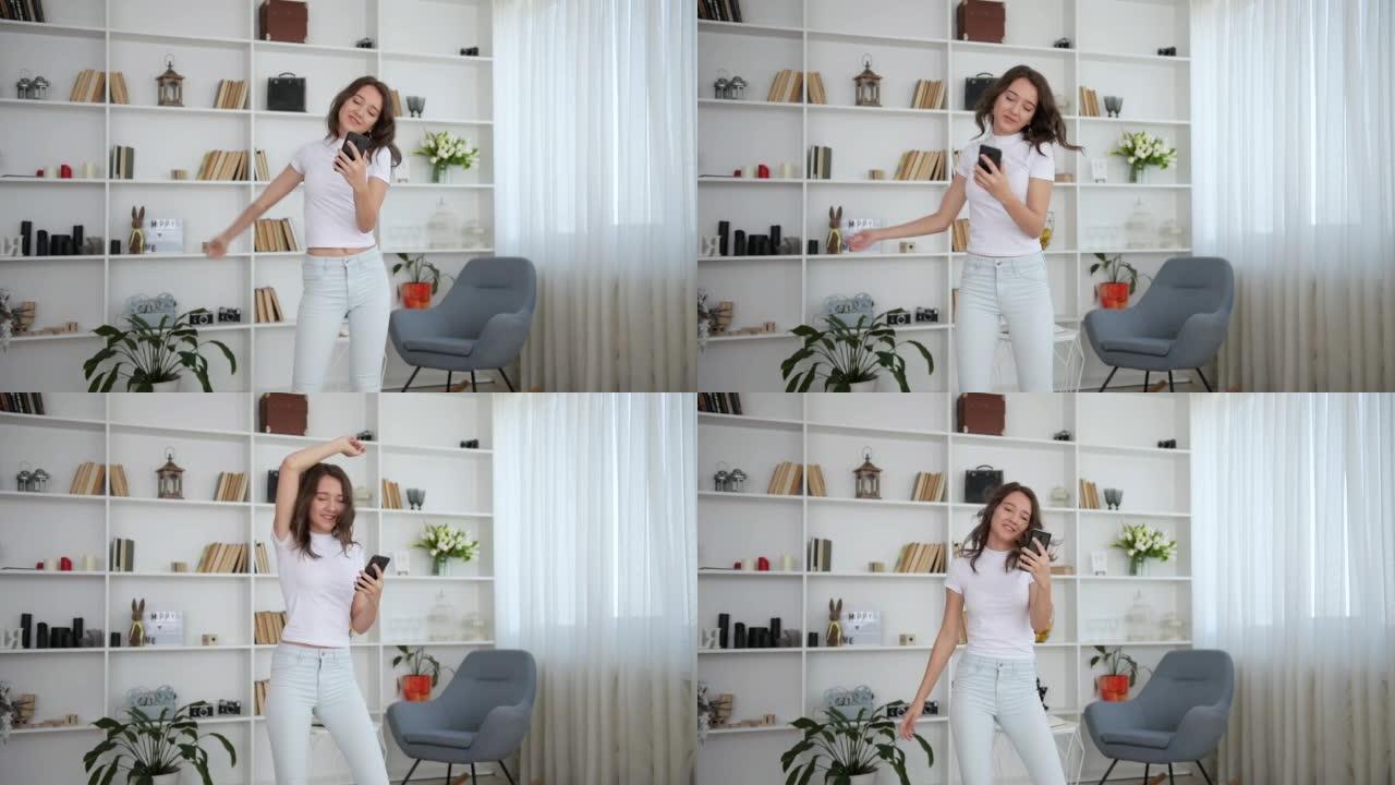 穿着白色衣服的年轻女孩手里拿着智能手机在室内跳舞