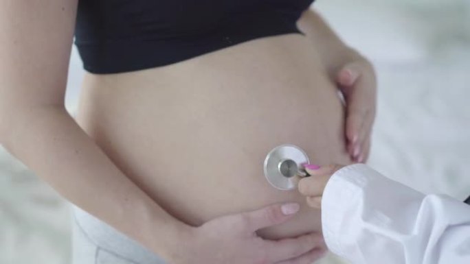 怀孕女性高加索腹部特写无法辨认的医生用听诊器听胎儿心跳。怀孕期间接受医学检查的年轻孕妇。