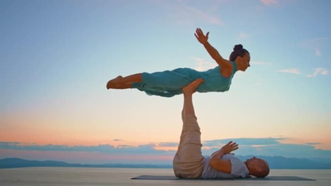 CS女人在日落时被她的瑜伽伴侣在山顶上举起