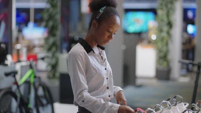 美国黑人女士正在数字设备商店购物，查看新型号的智能手表，并取样