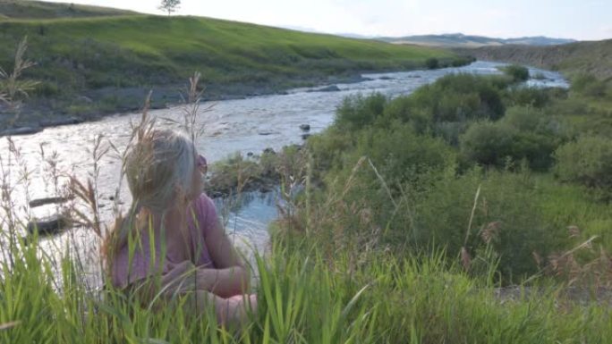 成熟的女人在河边的草丛中放松，远处的山脉