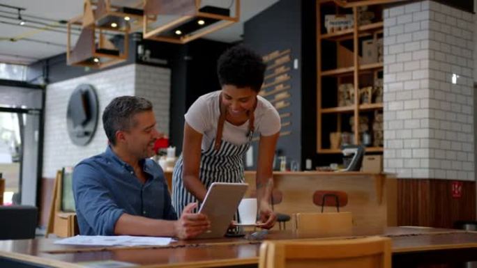 黑人友好的女服务员在咖啡店里为在平板电脑和文件上工作的商人提供咖啡