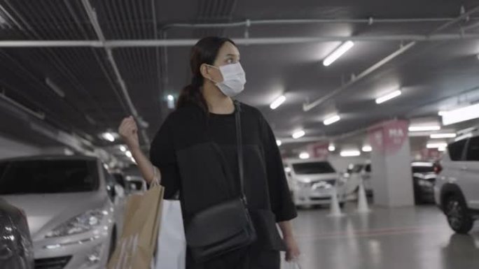 戴着口罩的女人带着购物袋在商场停车场醒来