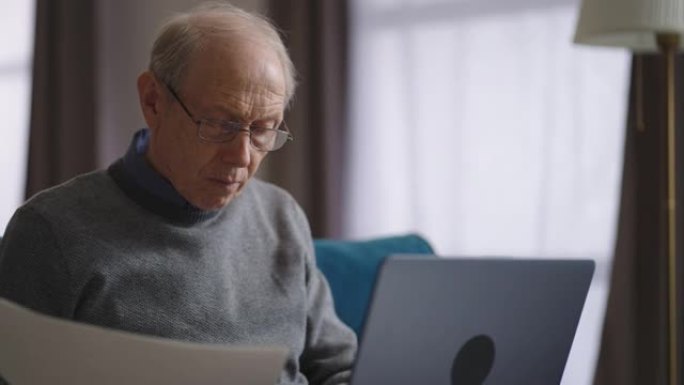 老人在家里工作，查看文件并使用笔记本电脑打字，是经验丰富的专家的远程工作