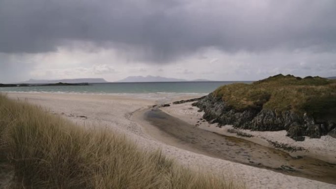 苏格兰的白色沙滩，河流流入大海，远处是多山的岛屿