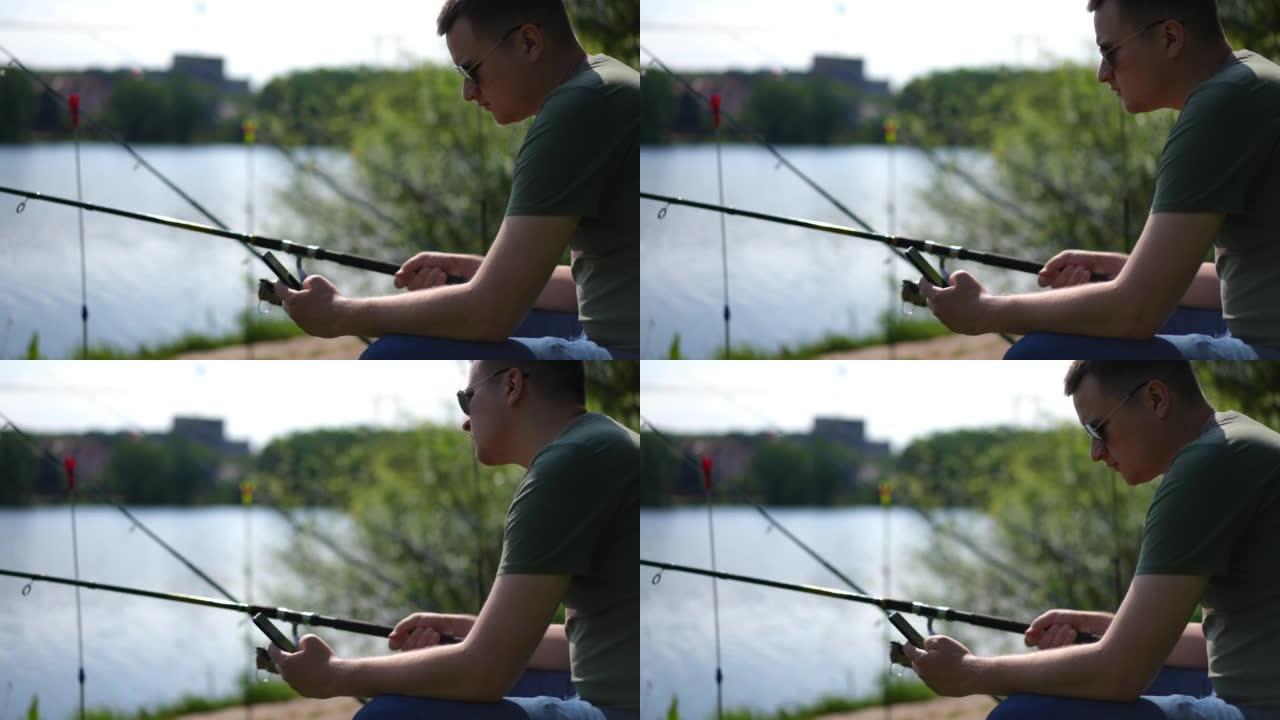 冷静自信的年轻渔夫在右侧滚动智能手机上的社交媒体，在阳光下看着河。夏季早晨，放松的高加索人用钓竿钓鱼