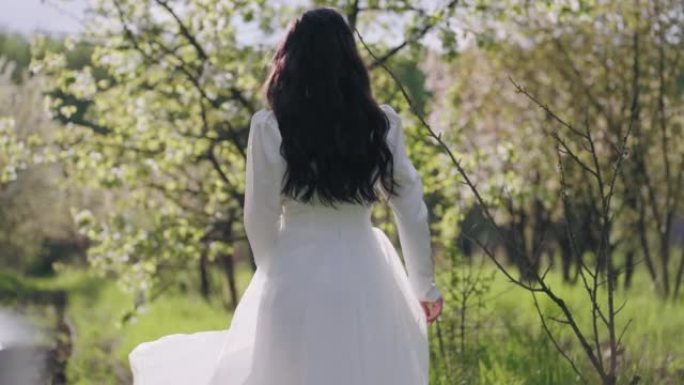 春天盛开的花园里美丽的新娘，穿着白色连衣裙的女性形象的后视图