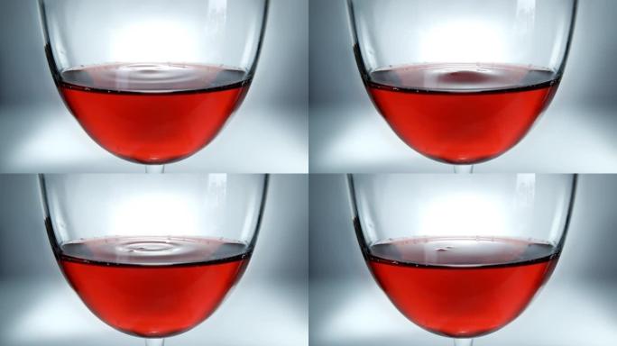 杯子里的红酒和落下的酒滴。酒滴在玻璃杯中慢慢落下特写。4k微距慢动作视频。在高速电影摄像机上拍摄。