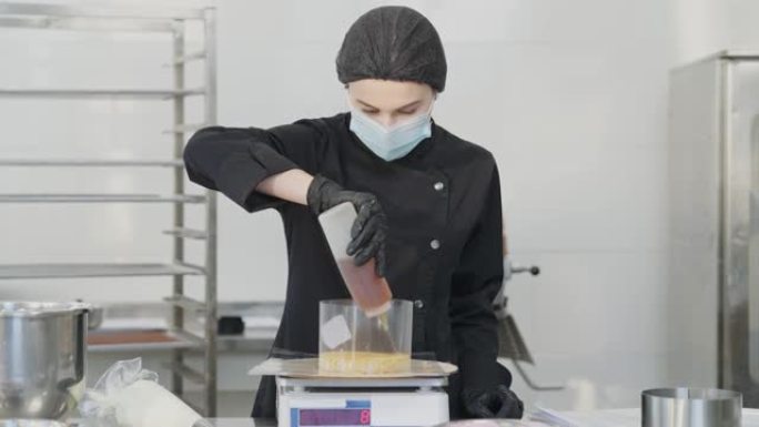 2019冠状病毒病的美丽浓缩女性面膜正面，将液体糕点糖浆浇在烤糕点面团上。年轻的白种人糕点师在厨房烹
