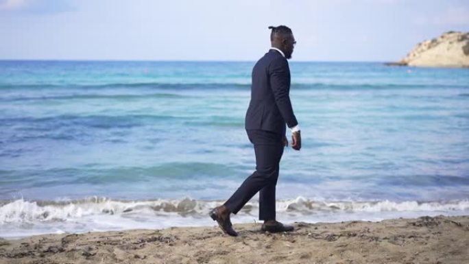 优雅的年轻非洲裔美国人在沙滩上漫步，绿松石蔚蓝的海浪以慢动作在海岸上滚动。风景如画的地中海海景，轻松
