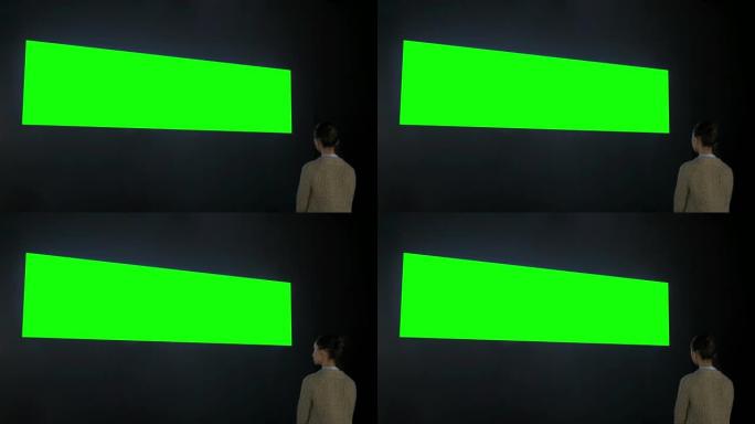 女人看着空白的宽互动墙显示-绿屏概念