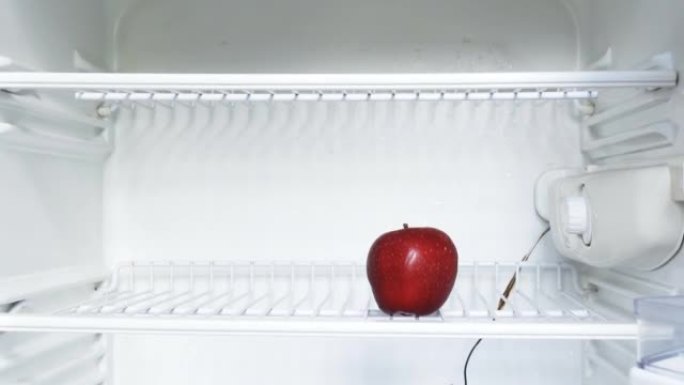 一个人的手打开一个空冰箱，拿了一个红苹果。概念性4k原始视频。经济危机、粮食短缺、贫困的想法。